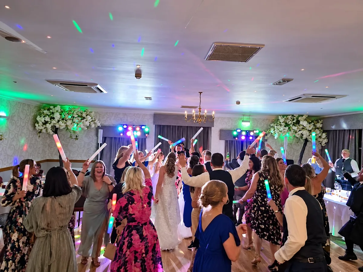 Wedding guests dancing with glow sticks around the bride and groom